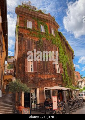 Italien, Rom - 03. April 2024: Altes Gebäude mit Bar im Erdgeschoss in Trastevere, mit Efeu bedeckt Stockfoto