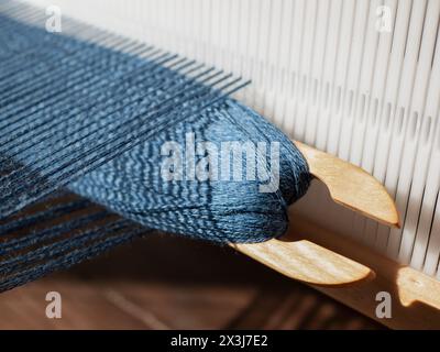 Holzwebefädel mit blauem Garn wird in offener Schuppen eingesetzt, selektiver Fokus. Trennung zwischen oberen und unteren Kettfäden, durch die der Schuss entsteht Stockfoto