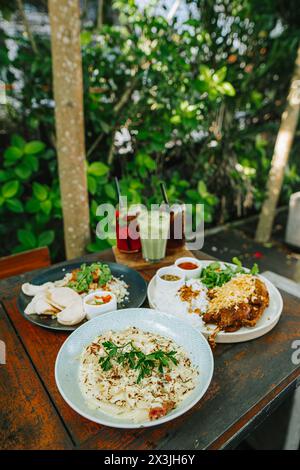 Indonesisch: Westliche Gerichte auf einem Holztisch zum Mittagessen. Konzentrierte sich auf Pasta mit verschwommenem, frittiertem Entenreis, gebratenem Reis und Cocktails Stockfoto