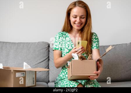 Happy Woman packt ihre Online-Bestellung aus, macht Fotos von ihren Einkäufen und teilt sie mit Freunden in sozialen Medien. Stockfoto