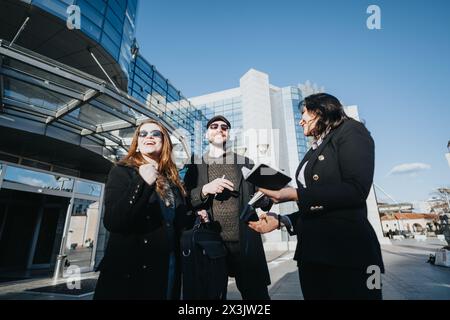 Drei junge Fachkräfte führten eine lebhafte Diskussion, tauschten Ideen aus und lächelten, während sie im Freien inmitten der Stadtarchitektur zusammenarbeiten. Stockfoto
