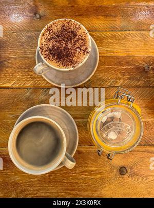 Cappuccino und schwarzer Kaffee neben einem Glas mit Zuckerwürfeln auf einem Holztisch in einem Café Stockfoto