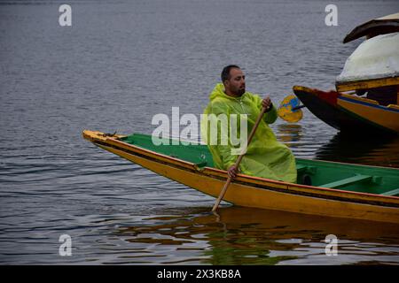 Srinagar, Indien. April 2024. Ein Mann mit Regenmantel rudert sein Boot nach starken Regenfällen in Srinagar über den weltberühmten Dal-See. In den nächsten 48 Stunden wird an den meisten Orten von Jammu und Kaschmir mit starken Regenfällen gerechnet. Auch über den höheren Talabschnitten ist mit moderatem bis starkem Schneefall zu rechnen. (Foto: Saqib Majeed/SOPA Images/SIPA USA) Credit: SIPA USA/Alamy Live News Stockfoto