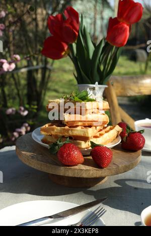 Frisch gebackene Waffeln und ein wunderschöner Tulpenstrauß auf dem Tisch im Garten Stockfoto