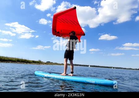 21. April 2024: Mann surft mit einem Flügelboot oder Windsegel auf einem SUP Board oder aufblasbarem Surfboard mit dem Wind im Wasser auf einem Badesee bei Sonnenschein *** Mann surft mit einem Wingfoil bzw. Wind-Segel auf einem SUP Board bzw. Aufblasbares Surfbrett mit dem Wind im Wasser auf einem Badesee bei Sonnenschein Stockfoto