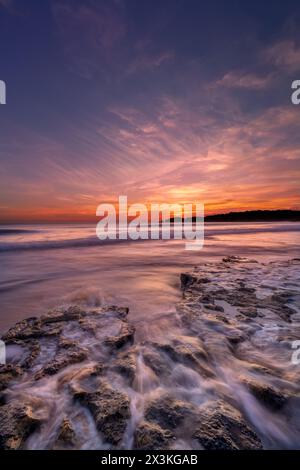 Wellen, die über Felsen an einem Strand in der Algarve in Portugal mit einem farbenfrohen Sonnenuntergang schweben Stockfoto