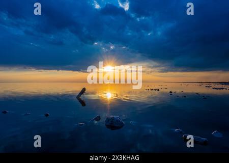 Atemberaubender Blick auf einen Sonnenuntergang über einem ruhigen See mit markanten Wolkenformationen und reflektierendem Wasser unter einem weiten Himmel. Stockfoto