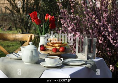 Wunderschöner Tulpenstrauß und frisch gebackene Waffeln auf dem Tisch, serviert zum Teetrinken im Garten Stockfoto