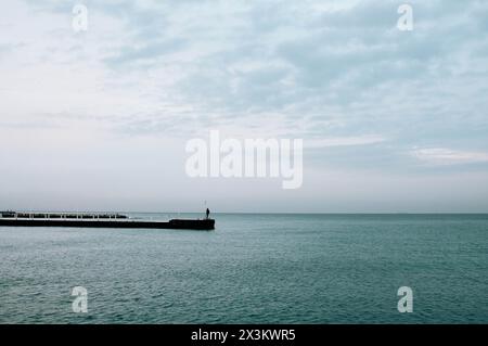 Ein Silhouettenmann, der auf dem Pier zum Meer hin steht Stockfoto