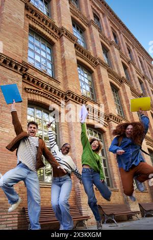 Glückliche Gruppe multiethnischer Schüler feiert den letzten Schultag, hüpft und hebt die Arme. Stockfoto