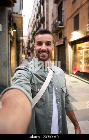 Junger Erwachsener glücklicher kaukasischer Mann, der ein lächelndes Selfie auf der touristischen Straße Madrids im Hintergrund macht. Stockfoto