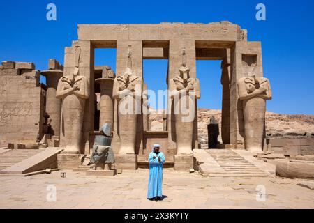 Ein ägyptischer Mann in traditionellem Attiire posiert vor den Osiride-Statuen des ägyptischen Pharao Ramesses II. Im Ramesseum in Luxor, Ägypten Stockfoto