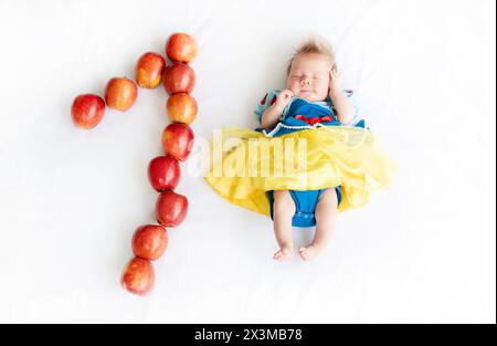 Flachbild eines einmonatigen Babys mit vielen Äpfeln. Neugeborenes Mädchen im Prinzessinnen-Outfit. Märchenkostüm auf einem Baby. 1 Monat alt mit einem n Stockfoto