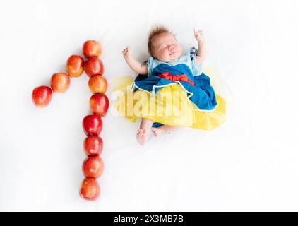 Flachbild eines einmonatigen Babys mit vielen Äpfeln. Neugeborenes Mädchen im Prinzessinnen-Outfit. Märchenkostüm auf einem Baby. 1 Monat alt mit einem n Stockfoto