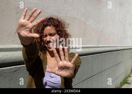 Lateinamerikanische, lockige Erwachsene Frau (34) mit positiver und lustiger Einstellung streckt beide Handflächen in ein hohes Zeichen. Lifestyle-Konzept. Stockfoto