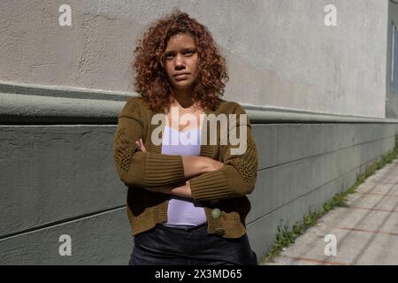 Lateinamerikanische Erwachsene Frau (34) afrikanischer Abstammung mit lockigen Haaren posiert mit überkreuzten Armen und ernster Haltung. Lifestyle-Konzept. Stockfoto