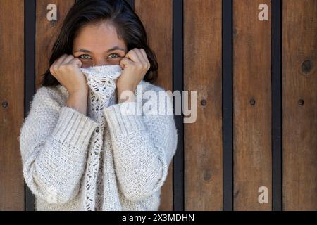 Lateinamerikanische Erwachsene Frau (29) lustig und spielend, sie bedeckt ihr Gesicht mit ihrem Pullover, nur ihre grünen Augen sind zu sehen. Lifestyle-Konzept. Stockfoto