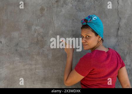 Lächelnde afro-lateinamerikanische Frau (34) mit Kopftuch, isoliert auf grauem Hintergrund, zeigt ihren Finger in den leeren Raum. Rabattangebot für Concept Promotion. Stockfoto