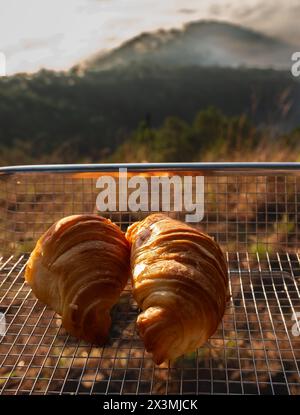 Croissants auf einem Tablett draußen. Sommer-Picknick am frühen Morgen in den Bergen. Picknick auf dem felsigen Berg bei Sonnenaufgang. Reisefoto, niemand Stockfoto