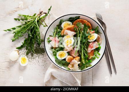 Frischer Sommersalat aus Löwenzahnblättern, Eiern, Speck und mit Brot auf hellem Hintergrund. Draufsicht Stockfoto