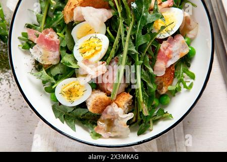 Frischer Sommersalat aus Löwenzahnblättern, Eiern, Speck und mit Brot auf hellem Hintergrund. Draufsicht Stockfoto