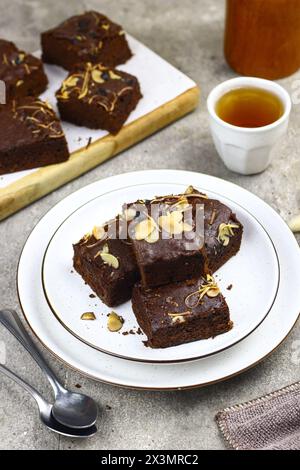 Brownies Scheiben auf weißer Keramikplatte, garniert mit geriebenem Mandel- und Cheddar-Käse. Teezeitkonzept mit grauem Hintergrund. Kopierbereich für Text. Stockfoto