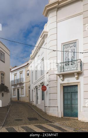 Enge kopfsteingepflasterte Straße in Tavira, Portugal, mit weißen Gebäuden und einem „No Entry“-Schild an der Ecke. Stockfoto