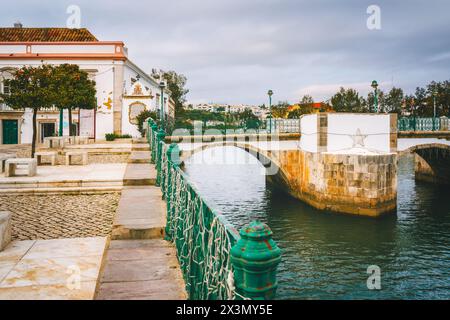 Die römische Brücke in Tavira, Portugal, mit weißen Geländern und Steinbögen, die über einen ruhigen Fluss führt. Stockfoto