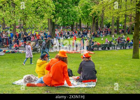 Drei Frauen sitzen auf einem Teppich im Gras und beobachten die Menschenmassen im Stadtpark Valkenberg in Breda während des Königstages 2024 aus der Ferne. ANP / Hollandse Hoogte / Ruud Morijn niederlande Out - belgien Out Stockfoto