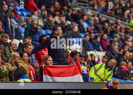 Ein Middlesbrough FC-Fan zeigt seine Unterstützung für sein Team, während er leidenschaftlich mit anderen Fans singt, während ein Steward zusieht. Cardiff City Stadium, Wales. Stockfoto