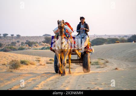 Kamelbesitzer, der auf einem bunten Wagen sitzt und auf einem Pfad im Sand nach Touristen sucht Stockfoto