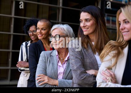 Seitenansicht. Das GROUP Lächeln befähigte verschiedene formelle Geschäftsfrauen, die mit überkreuzten Armen im Freien standen. Stockfoto