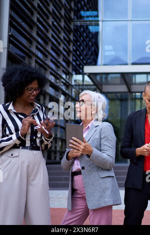Vertikal. Team multikulturellen Geschäftsfrauen in formeller Kleidung, die mit einem Mobiltelefon stehen und aussehen Stockfoto