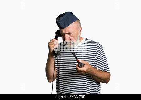 Ein alter Seemann aus der Vergangenheit spricht am Telefon. Porträt auf weißem Hintergrund. Seemann mit einer rauchenden Pfeife und einem alten Telefon in der Hand Stockfoto