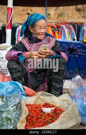 Schwarze Hmong-Frau verkauft Chilis auf dem Cau-Markt in Lao Cai, Vietnam Stockfoto