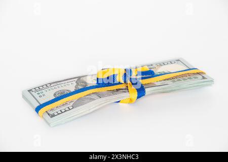 Band in Form der Flagge der Ukraine, gebunden in einer Schleife auf einem Stapel von hundert Dollar-Scheinen auf weiß, finanzielle Hilfe für die Ukraine Stockfoto