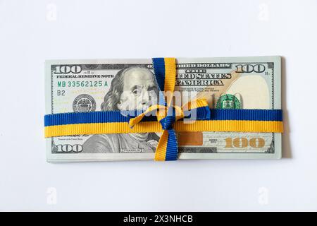 Band in Form der Flagge der Ukraine, gebunden in einer Schleife auf einem Stapel von hundert Dollar-Scheinen auf weiß, finanzielle Hilfe für die Ukraine Stockfoto