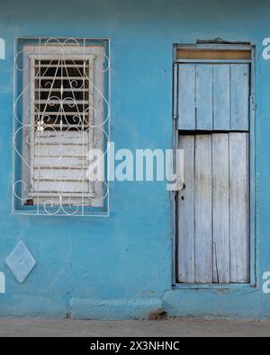 Haus mit einer Holztür und einem dekorativen Metallgitter über den Fenstern in den Seitenstraßen der Altstadt, Trinidad, Kuba. Stockfoto
