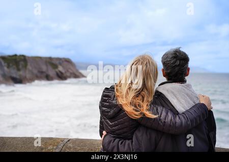 Eine Rückansicht eines schwulen Frauenpaares, das sich an einem Pier umarmt und in den Horizont blickt. Die Szene ist romantisch und schön Stockfoto