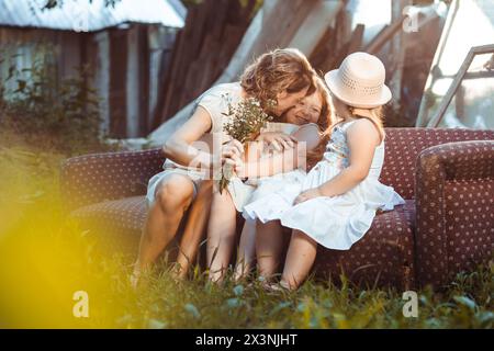 Die junge Mutter mit ihren beiden Töchtern sitzt draußen auf der Couch. Muttertag Stockfoto