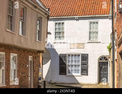 Ein weiß getünchtes Haus, das in der Sonne gefangen ist, befindet sich an der Kreuzung zweier schmaler Gassen. Das untere Fenster hat einen alten Satz von Rollläden und eine Tür auf einer Seite. Stockfoto