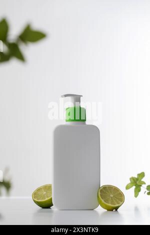 Eine elegante weiße Shampoo- oder Duschgel-Flasche mit einer leuchtend grünen Pumpe und frischen Limettenscheiben. Hautpflege Stockfoto