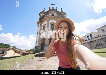 Selfie-Mädchen in Ouro Preto, Brasilien. Junge Touristenfrau, die Selbstporträt mit der Kirche unserer Lieben Frau vom Rosenkranz im touristischen Reiseziel Ouro Preto macht Stockfoto