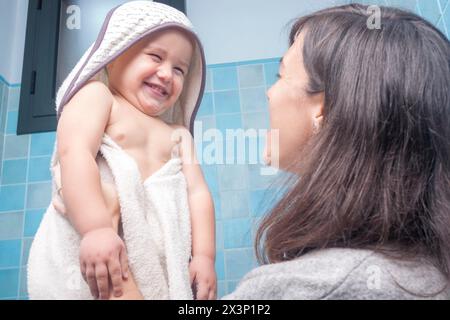 Mutter holt ihren mit Handtüchern umwickelten Sohn nach einer Dusche ab Stockfoto