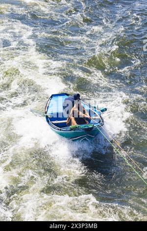 Zwei ägyptische Männer in einem Ruderboot, die einen Schlepper von einem vorbeifahrenden Nilschiff nehmen. Nil, Ägypten Stockfoto