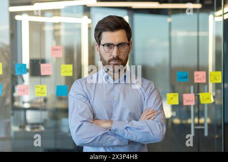 Ein Mann in einem blauen Hemd steht vor einer Wand, die mit gelben und rosa Haftnotizen bedeckt ist Stockfoto