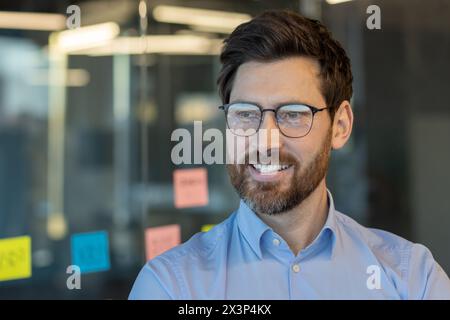 Ein Mann mit Brille und blauem Hemd lächelt vor einer Wand mit bunten Haftnotizen Stockfoto