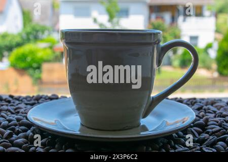Grüne Tasse Kaffee und geröstete Kaffeebohnen auf der Fensterbank. Stockfoto