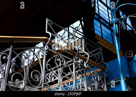 Geschmiedetes Treppengeländer auf einem Markt in Budapest, Ungarn, am Fővám-Platz. Blaue Wände und hölzerne Handläufe. Ein blauer Kandelaber. Stockfoto