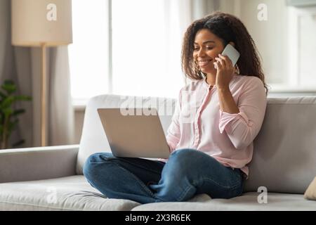 Frau, die mit einem Anruf am Arbeitsplatz beschäftigt war, während sie einen Laptop auf dem Sofa benutzte Stockfoto